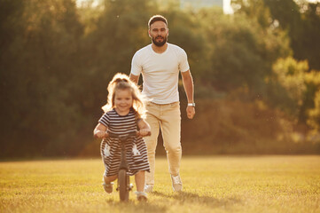 Fototapeta premium Riding the bicycle. Father with his little daughter are on the field