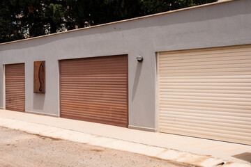 Two garage doors in different colors, one brown and one beige, set against a gray wall with a stone accent.
