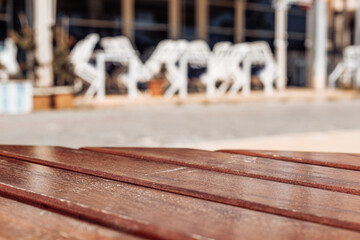 A close-up of a wooden table with a blurred background of white chairs in a cafe setting. The scene conveys a relaxed outdoor dining atmosphere.