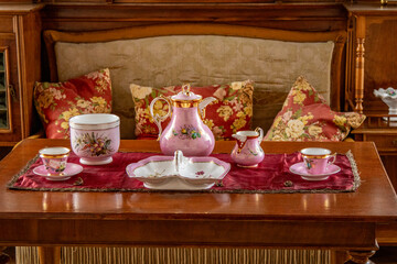 Vintage pink porcelain tea set on a wooden table with red velvet runner