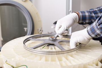 Fastening washing machine pulley during repair. Hands in white gloves tighten a nut on a washing machine pulley with a wrench