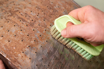 Cleaning a rusted metal surface of washing machine drum with a brush. A hand with a brush cleans an old metal surface of washer drum covered with layer of lime calx of hard water