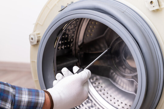 Washing machine repair: drum inspection. A hand with a screwdriver near the open washing machine drum, the process of appliance repair or maintenance