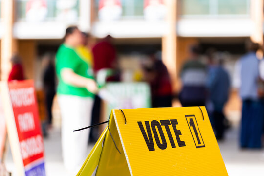 vote 1 on sign with out of focus voters waiting to enter polling station