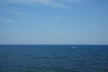 Obraz premium Blue sea with small boat on the horizon under clear sky. Minimalist seascape background, perfect for travel, freedom, and relaxation themes