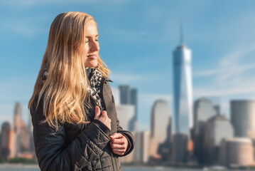 Pretty woman looking at skyscrapers and skyline during her trip. Woman with long blonde hair in black jacket standing in front of city skyline and skyscrapers