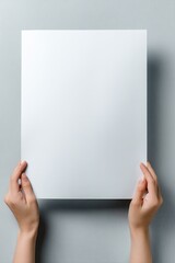 Blank white sheet of paper held by hands against a neutral backdrop
