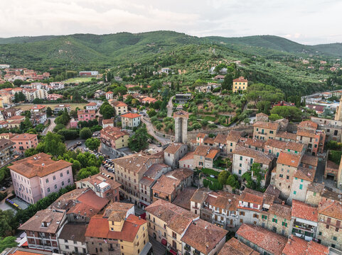 Aerial view of terracotta rooftops cascade down to meet the ancient tower, embraced by verdant hillsides, Passignano sul Trasimeno, Umbria, Italy.