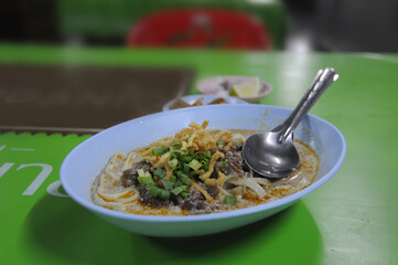 A bowl of Khao Soi. It is a Thai egg noodle soup in a curry broth, topped with crispy fried noodles.