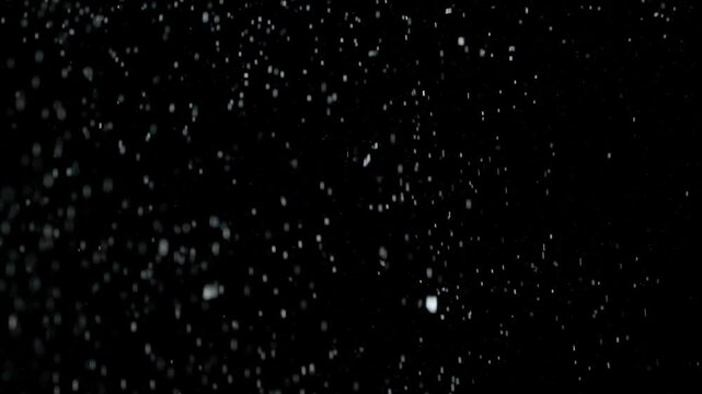 Many silver glitter particles powder falling from above, floating on empty black contrast background. Slow motion.