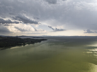 Aerial view of where the land kisses the tranquil lake under a sky heavy with brooding clouds near Trasimeno Lake, Torricella, Umbria, Italy.