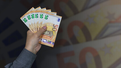 A male hand holding 50 Euro bills on an unfocused background.