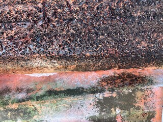 Close-up of a weathered concrete surface with textured black mold, orange rust stains, and green...
