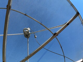 Close‑up view of a satellite TV dish antenna with metal mesh and structural frame against a clear blue sky, highlighting details of technology and construction.