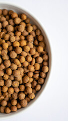 Close up of a white bowl filled with dried brown lentils on a white background