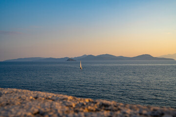 Sailboat at sunset on a calm sea with distant mountains
