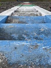 Weathered concrete steps painted blue, white, and multicolor lead upward through rocky terrain, showing texture, age, and outdoor path design.