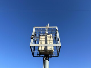 Close-up of a secured wireless communication antenna in a protective metal cage against a bright clear blue sky on a sunny day.