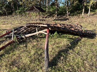 Collapsed wooden hut with broken roof tiles lying on dry grassy ground near a forest, depicting decay, abandonment, and the passage of time.