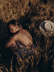 Portrait of young sunlit woman in white bra relaxes on field among ripe ears of wheat.