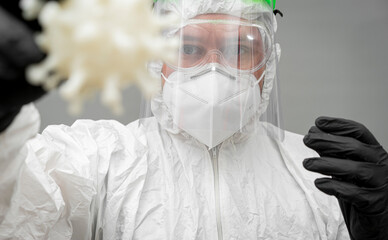 Medical professional examines a covid-19 virus model while wearing full protective gear in a...