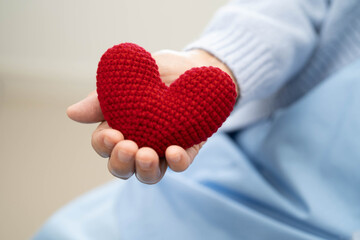 Asian elder senior woman patient holding red heart in hospital.