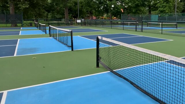 Outdoor Pickleball Courts. Sweeping views in motion of empty pickleball courts. Moving backwards across several courts in a row. Public city park setting with cloudy blue Summer sky.