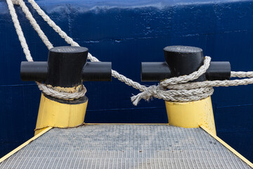Yellow Black Mooring Bollards with Maritime Ropes Against Blue Hull Background