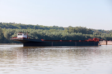 A large cargo ferry navigating calm waters of a river with a forested background