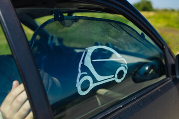 A man sitting in a small modern car, captured from the open driver's door with a scenic rural background. Concept of eco-friendly transportation, travel, and exploration in nature.