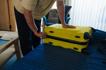 Traveler preparing for a trip indoors by packing a bright yellow suitcase on a bed in a cozy room. Casual scene of planning and organizing essentials for an upcoming vacation or business journey