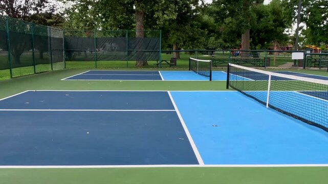 Outdoor Pickleball Courts. Sweeping views in motion of empty pickleball courts. Moving forward across several courts in a row. Public city park setting with cloudy blue Summer sky.