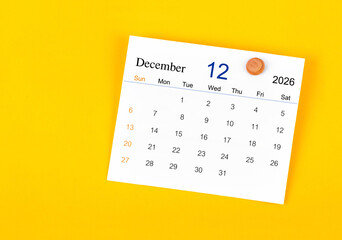December 2026 card calendar and wooden push pin on yellow color wall.