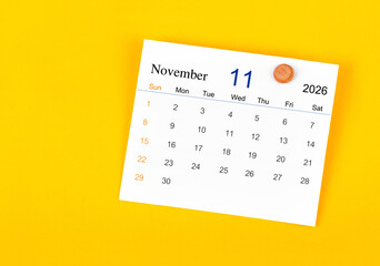 November 2026 card calendar and wooden push pin on yellow color wall.