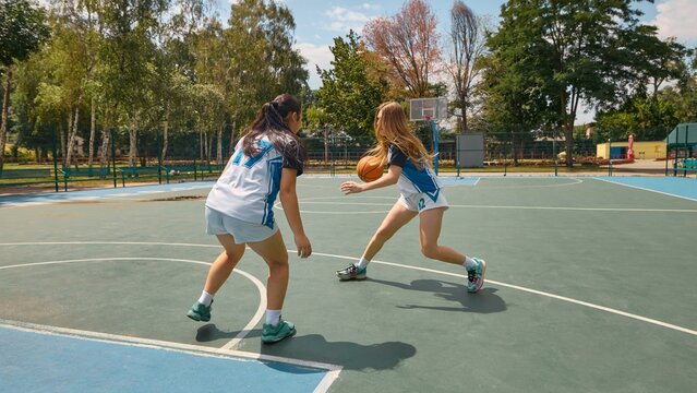 Women basketball players compete on an outdoor court under clear blue sky. Concept of sports competition, female strength and confidence, youth rivalry visuals, promotional content for girls in sport
