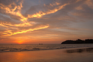 A vibrant sunset paints the sky with orange and yellow hues over a tranquil beach, creating a serene and picturesque scene.