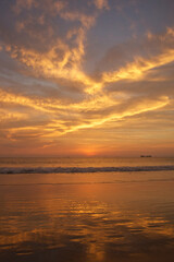 A beautiful sunset over the ocean, with golden clouds reflecting on the wet sand.