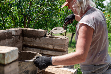 Man applying cement mortar to bricks to build a brick oven barbecue in the backyard, home...