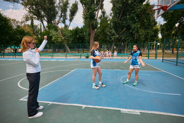 Referee signaling during basketball game with teen players reacting emotionally on court. Concept of youth sports rules, emotional competition, school match, coaching in summer sport.