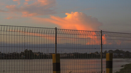 Sunset Over River With Fence And Structures