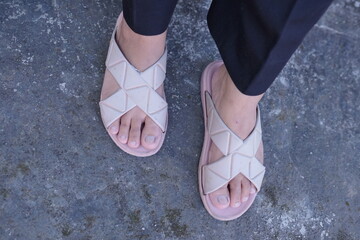 A minimalist overhead view of a person's feet in chic beige criss-cross sandals on a textured grey...