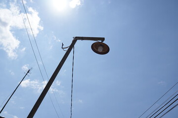 A low angle view of a vintage street lamp against a bright blue sky with the sun shining brightly, creating a sun flare.