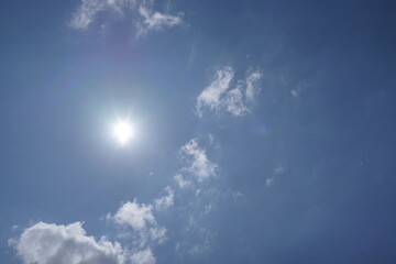 Expansive blue sky with a radiant sun and soft, ethereal clouds, a perfect summer day.
