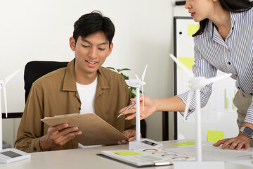 Sustainability. Young professional reviewing renewable energy plans with wind turbine models.