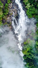 Breathtaking Top View of Waterfall Flowing Through Lush Green Jungle with Fog