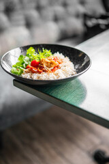 Colorful vegetarian rice bowl with cherry tomatoes, herbs, and vegetables served in a black dish on wooden table, top view, healthy homemade meal.