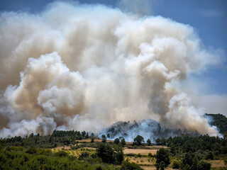 Incêndio florestal numa zona montanhosa com densa fumaça no ar e chamas intensas a queimar toda a floresta