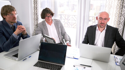 Three entrepreneurs are sitting at a table with their laptops open in front of them. Meeting of the...