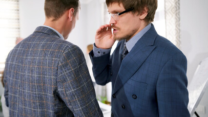 A serious, personable boss gives instructions to his assistant. Two men in suits are talking to...