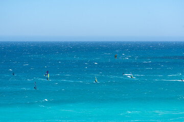 Zahlreiche Windsurfer und Kitesurfer sind auf dem leuchtend t&uuml;rkisfarbenen Wasser unter einem weiten, blauen Himmel aktiv